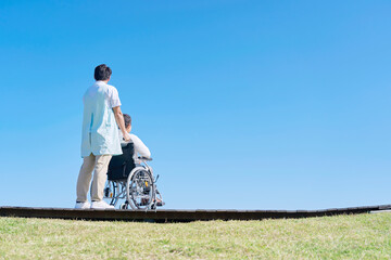 看護師と屋外を車椅子に乗って散歩する高齢者女性の後ろ姿