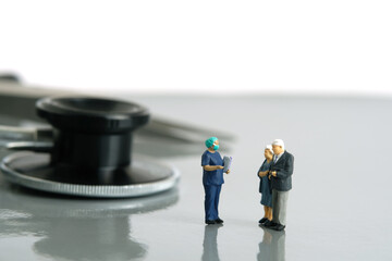 Miniature people toys conceptual photography. Elderly couple talking with surgeon doctor or nurse discussing post surgery result diagnosis, standing in front of stethoscope