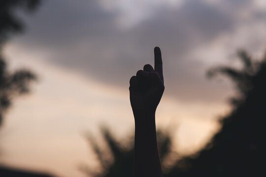 Silhouette of people pointing finger or making number one hand sign with blurred sunset sky background