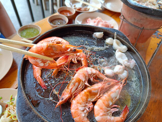 woman asia hand holding chopsticks grilled shrimp on a hot pan, on a wooden table