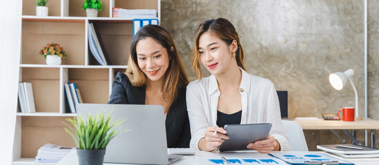 Beautiful Asian business office woman looks interested in online content on portable tablet with her college friends.