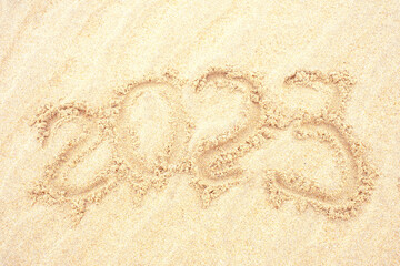 Inscription 2023 on golden sand close-up, top view