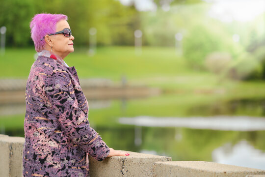 Funny Aged Woman With Short Pink Hair And Woolen Coat Standing By The River Embankment