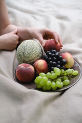 Fresh fruits on the plate on the blanket outdoors in the park. Summer grape, peach, melon. Picnic with colorful food on the grass. Copy space.