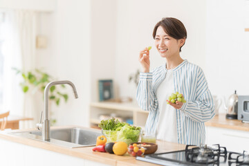 キッチンでフルーツを食べている健康的な日本人女性