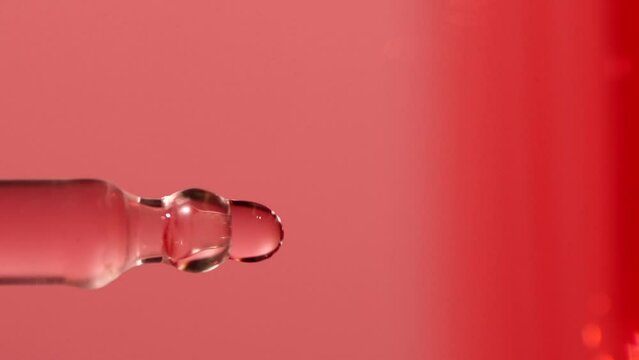 Slow motion of pink serum fluid, oil drop falling from dropper, pipette in water