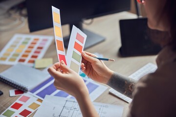 Close up shot of hands of female interior designer working on a project, holding color samples, sitting at the desk in her office