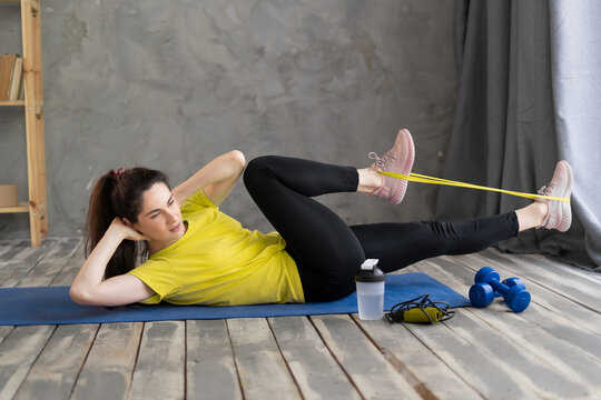 woman doing fitness at home with resistance rubber band, exercises for legs and ass lying on the floor, sport and fitness