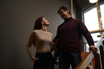 Successful creative team of a handsome man and a beautiful woman - business partners, colleagues, couples, met on the stairs in a cozy office interior