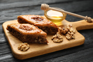 Delicious sweet baklava with walnuts and honey on black wooden table, closeup