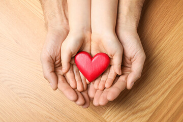 Fototapeta premium Man and kid holding red heart in hands at wooden table, top view