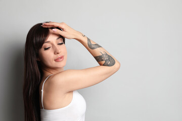 Fototapeta premium Beautiful woman with tattoos on arm against grey background. Space for text