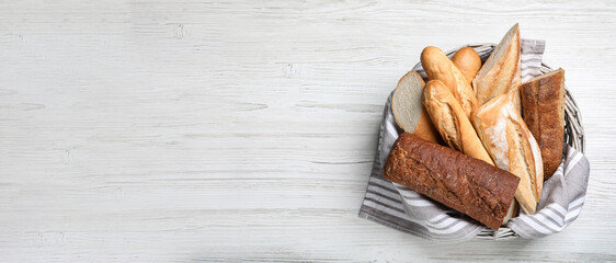 Different tasty baguettes in basket on white wooden table, top view with space for text. Banner design