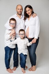 Family with Children over White background. Father and Pregnant Mother with Kids happy smiling embracing together. Parents and two Sons looking at camera standing over Gray