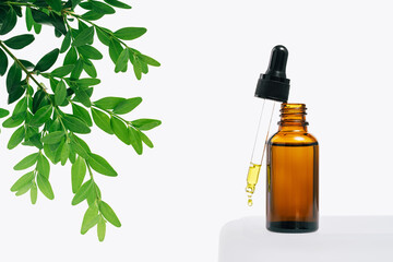 Natural medicine or aroma oil or beauty essence concept mockup vial with dropper with droplet on glass stand with green plant and white background. Face and body spa serum care concept banner