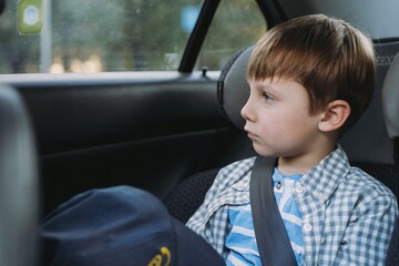 Cute little Caucasian boy sitting in child seat travelling by car tired and bored