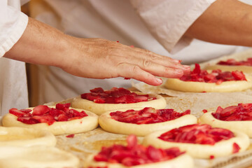Obraz na płótnie Canvas Baker makes filled pies from yeast dough, filling pies with strawberries. Work in bakery. Selective focus.