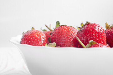 close-up of strawberries that lie in a plate on a white wooden background