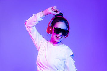 Young asian woman in white crop shirt wearing sunglasses and red headphone dancing on the purple...
