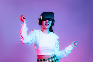 Young asian girl in white sweatshirt wearing vr headset watching playing and dancing on the purple screen background.