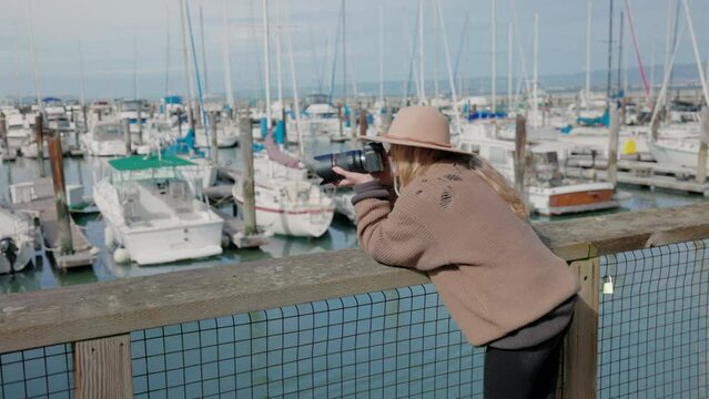 Solo traveler enjoys her vacation at the coastal city. Back view of a female photographer takes pictures of yachts and boats in the docks. High quality 4k footage