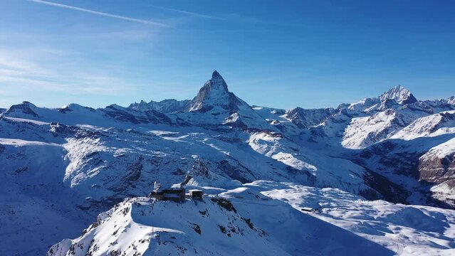 Picturesque winter Alpine landscape of snow-capped rocky ridge Gornergrat with observatory on summit and high pyramidal Matterhorn mountain in background on sunny day, Switzerland