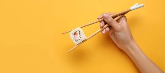 Fotobehang Hand holding chopsticks with delicious sushi roll on yellow background with space for text © Pixel-Shot