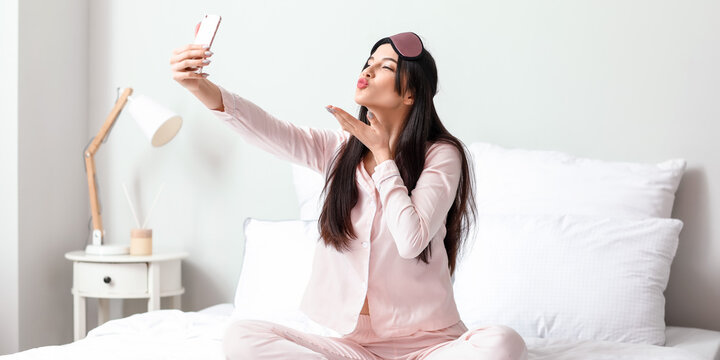 Pretty young woman taking selfie in bed
