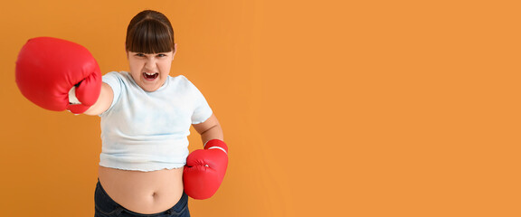 Aggressive overweight girl with boxing gloves on orange background with space for text - obrazy, fototapety, plakaty