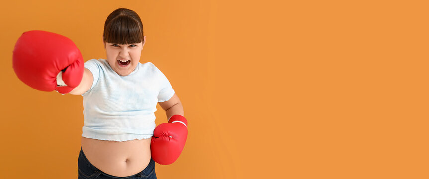 Aggressive overweight girl with boxing gloves on orange background with space for text