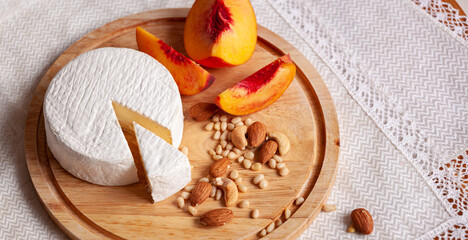 Young homemade Camembert Cheese on wooden dish with nuts and peach. Selective focus