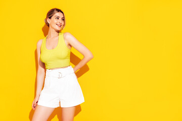 Young beautiful smiling female in trendy summer shorts and top clothes. Sexy carefree woman posing near yellow wall in studio. Positive model having fun and going crazy. Cheerful and happy