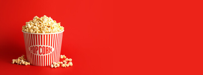 Bucket with tasty popcorn on red background with space for text - obrazy, fototapety, plakaty