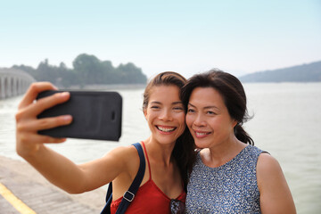 Mother adult daughter traveling together in Asian taking selfie picture with mobile phone. Smiling Asian family outside - Powered by Adobe
