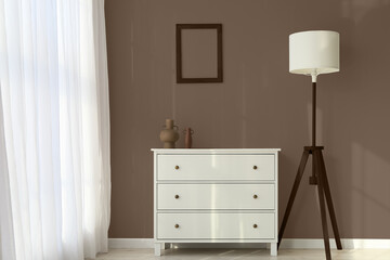 Chest of drawers and lamp near brown wall in modern room