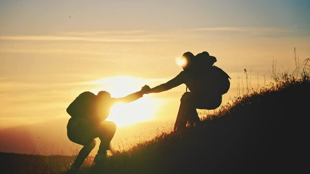 Silhouette of a helping hand to the man mountaineer. Two hikers on top of the mountain, a man helps a man to climb. Two hiker helping on hiking trail to summit the top of mountain. Teamwork concept.