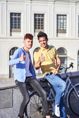 Fototapeta na wymiar Young gay couple holding a gay pride flag while riding a bike outdoors. LGBT, relationship and equal rights concept.