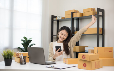 Happy Young asian entrepreneur woman checking product on smartphone. Business woman working SME online at home. Check address on parcel. Small business owner start up freelance concept.