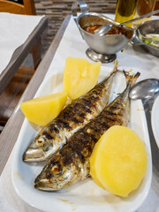 Grilled fish on a plate with boiled potatoes and red sauce in a dish