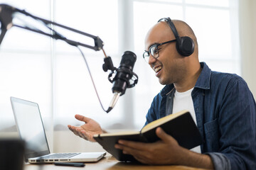 Content creator asia man host streaming his a podcast on laptop with headphones and condenser microphone interview guest conversation at home broadcast studio. Male blogger recording voice over radio