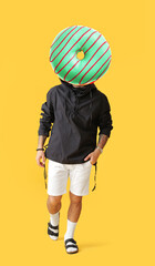 Fototapeta premium Stylish tattooed man with tasty doughnut instead of his head on yellow background