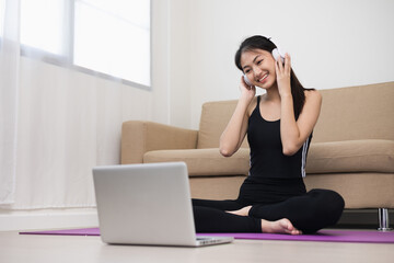 Young asian sport woman sitting practicing yoga lesson. Stretching leg training workout at home for good health and body shape. Learning skill form video online class by laptop.