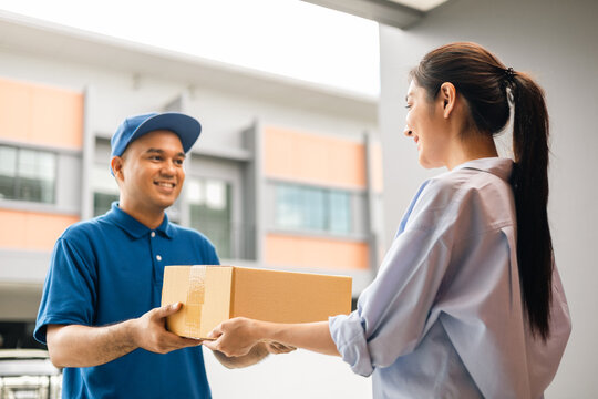 Beautiful Young Woman receiving parcel from blue uniform delivery man f the house with good service from shopping online. Courier man delivering a cardboard box postal package to destination.