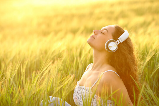 Woman meditating listening to music at sunset in a field