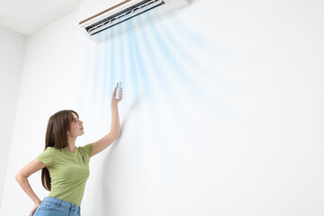 Pretty young woman switching on air conditioner in room