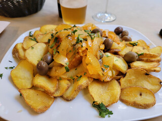 A plate of fried potatoes and bacalau fish with a beer