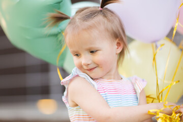 Fototapeta premium Funny girl child toddler with two tails with balloons outside. Balloons of pastel delicate colors