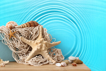 Starfish, sea shells and pebbles on table near wall with print of clear blue water