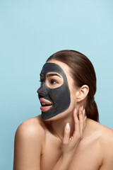 Beautiful  woman with facial  black mask touches her face.  Beauty  Skin care concept. .Girl  model with сosmetic mask .  Spa treatment . Cosmetology
