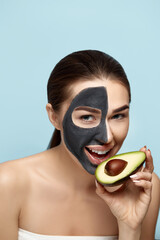 Beauty Facial Mask . Beautiful Young Woman with black mask of clay on face .Skin care .Girl beauty model with avocado in hand . Cosmetic  spa mask . Facial treatment